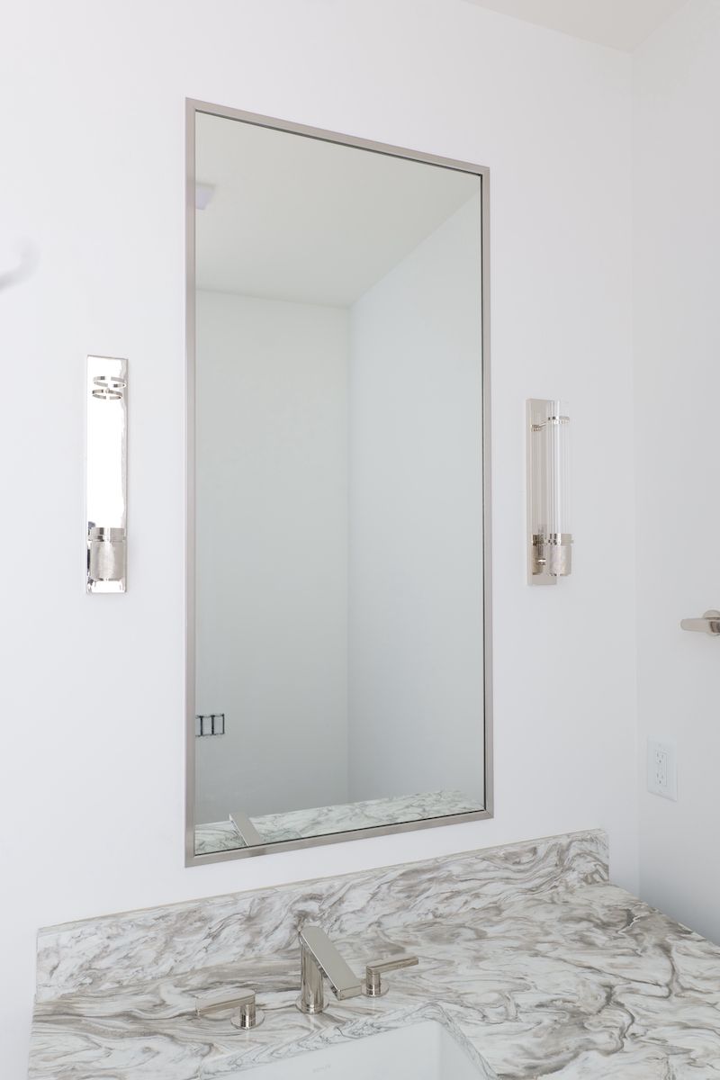 Bathroom with large rectangular mirror, silver frame, marble countertop, and sconce lights.