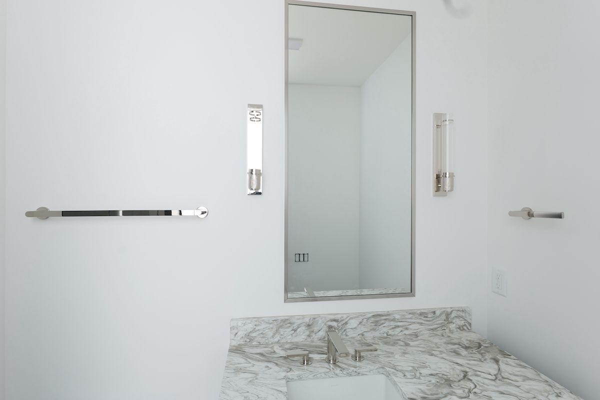 White bathroom with marble countertop, mirror, towel rack, and sconces.
