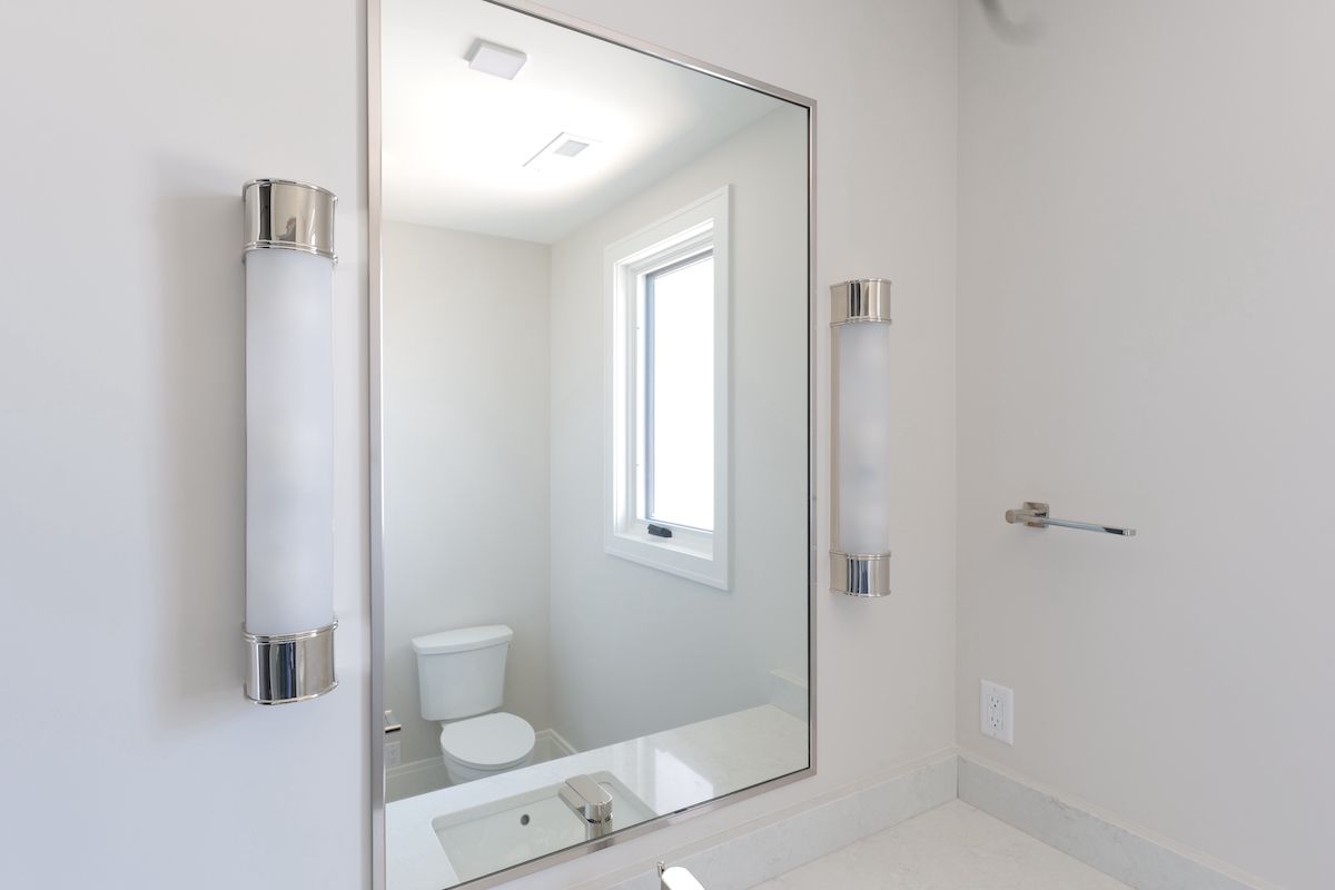 Bathroom with a large mirror, two wall sconces, a toilet, a window, and a sink.