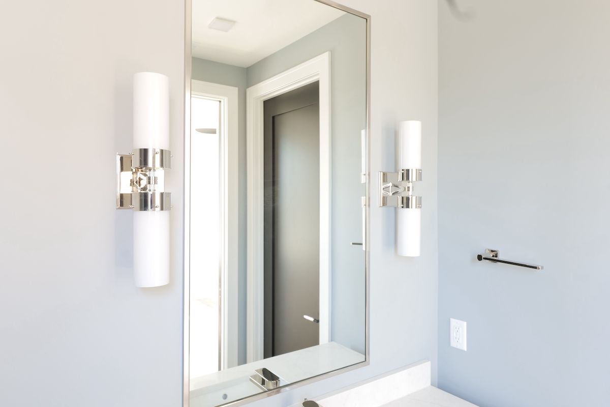 Bathroom with a large mirror, sconce lights, and a door, all set against a light gray wall.