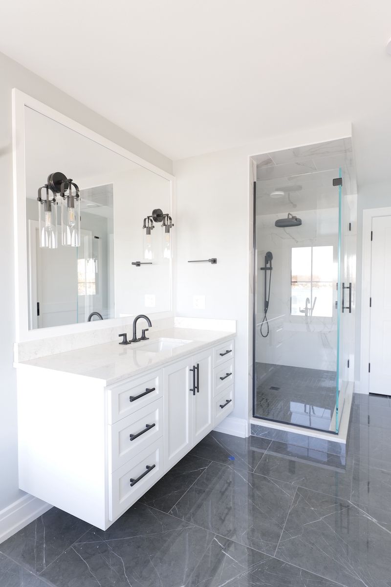 Modern white bathroom with floating vanity, glass shower, and gray floor tiles.
