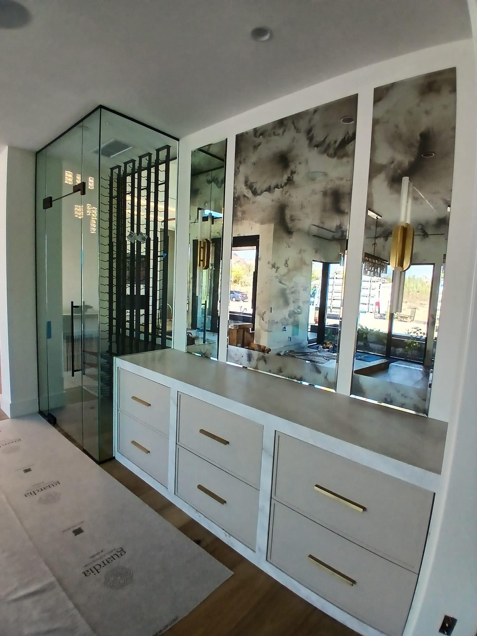Modern walk-in closet with cream-colored drawers, distressed mirrors, and a glass shower.