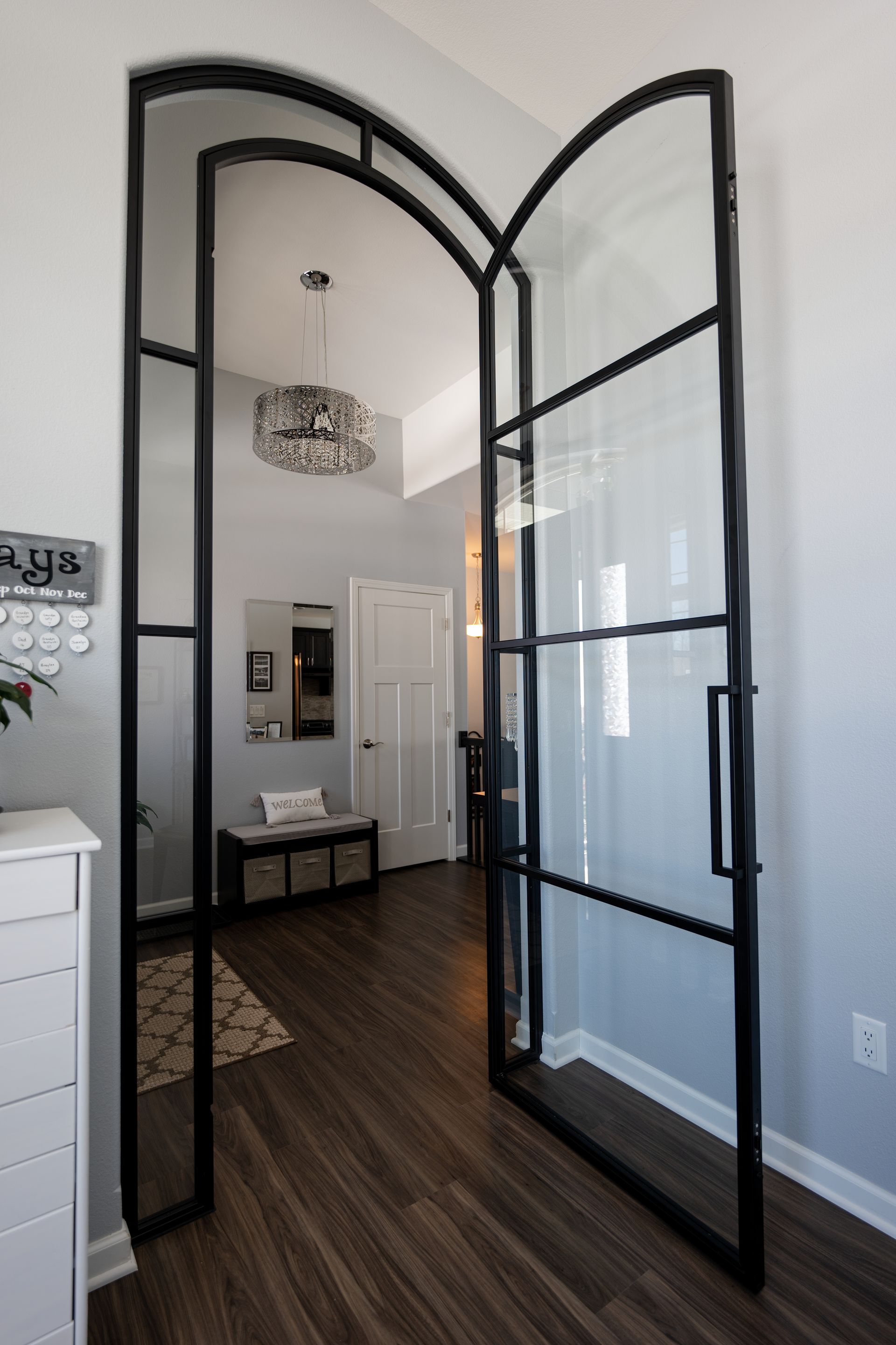 Open black metal-framed glass doors leading into a well-lit hallway with dark wood flooring.