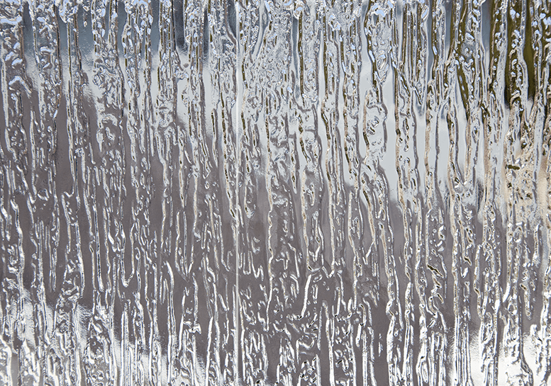 Textured, frosted glass with vertical, irregular striations reflecting light.