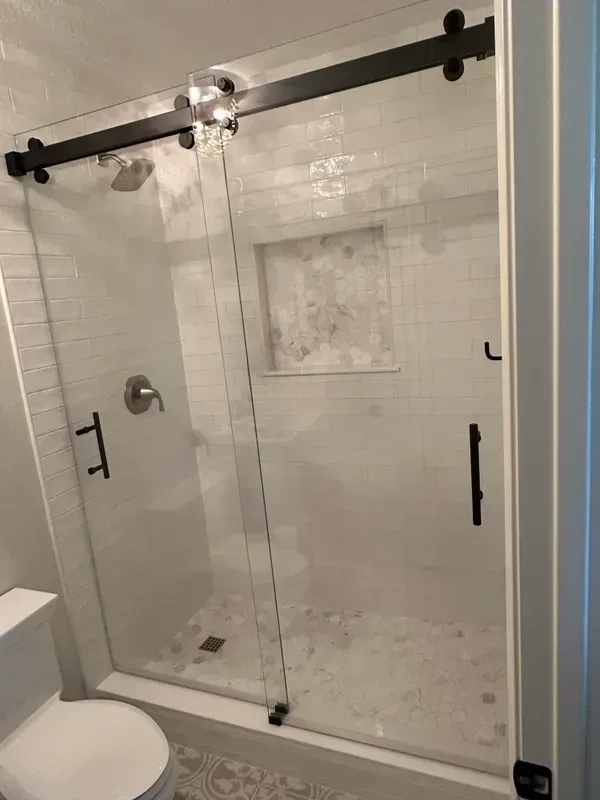 Modern shower with sliding glass doors, black hardware, white tile, and a built-in shelf.