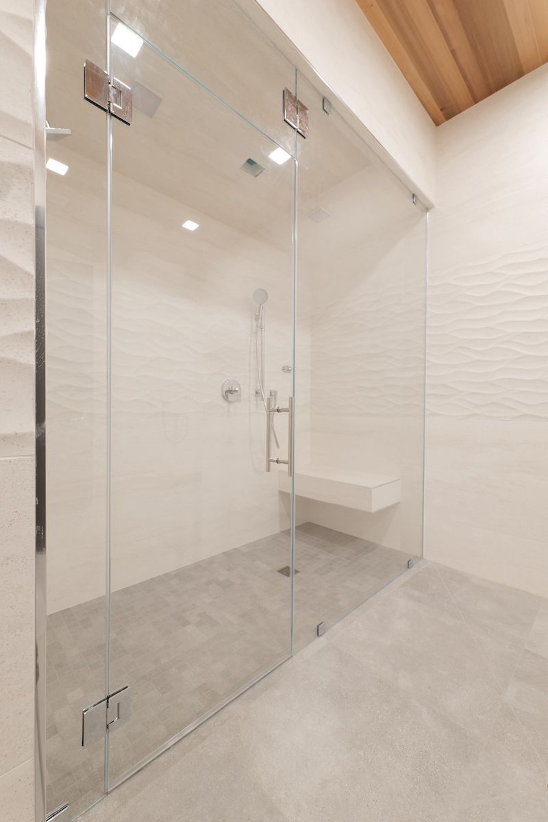 Glass shower enclosure in a modern bathroom with white tile and concrete floor.