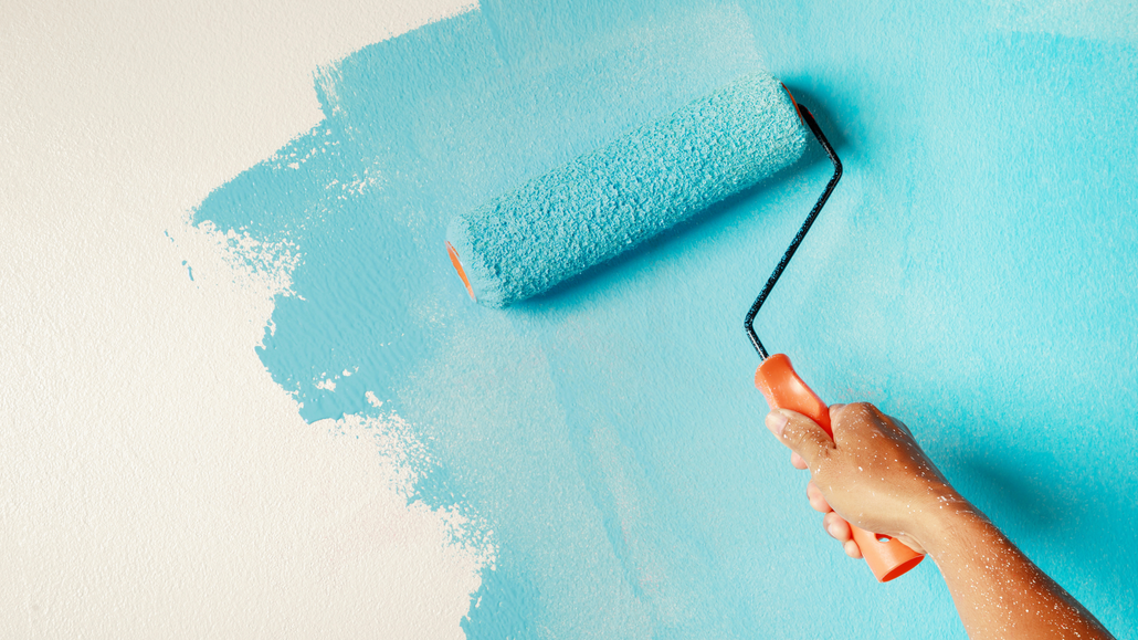 a person is painting a wall with a blue paint roller .