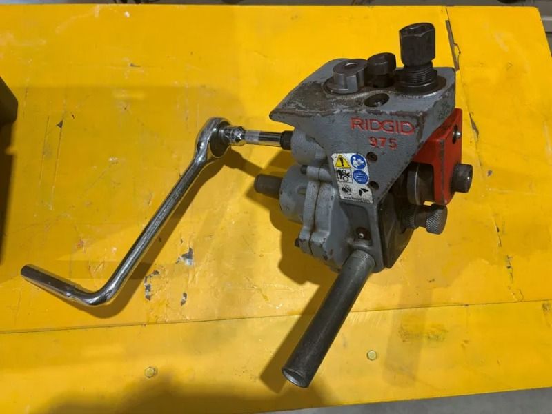 Red RIDGID pipe threading machine with crank handle on a yellow workbench.