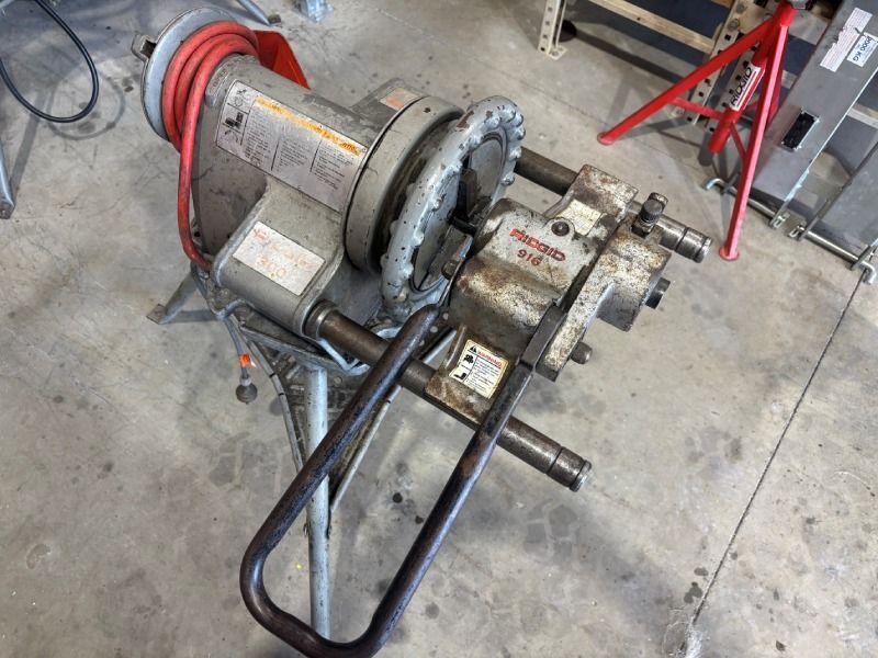 Industrial motor and pump assembly on a concrete floor with black tubing and a red cable reel.