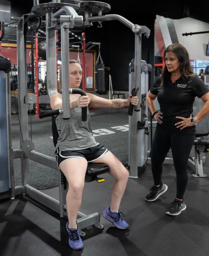 A woman is using a machine in a gym while another woman watches