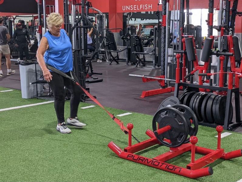 A woman is pulling a weight sled in a gym.