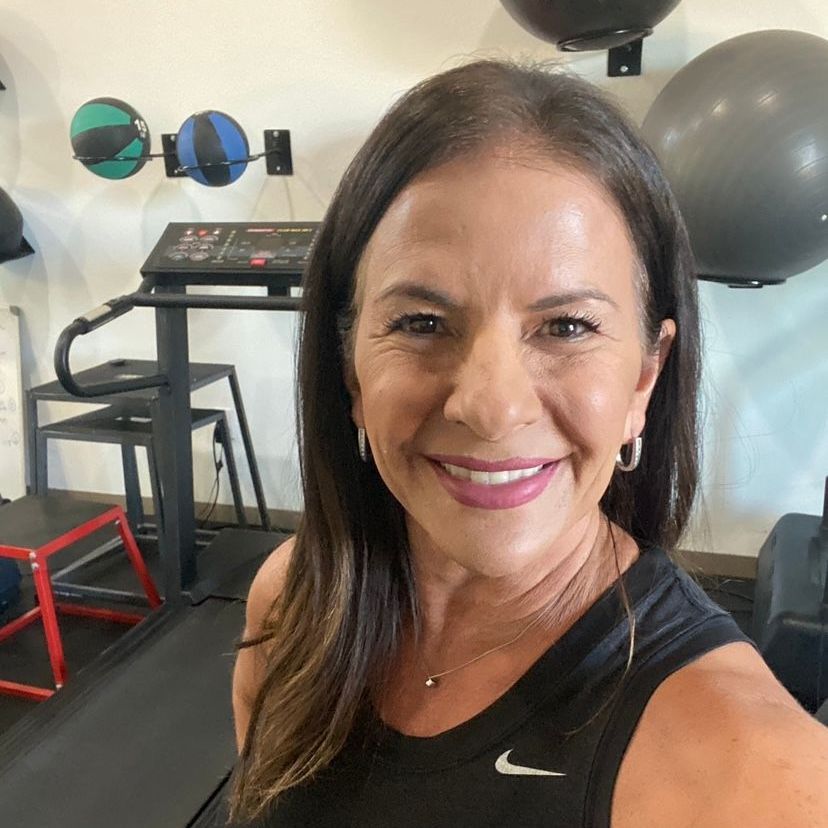 A woman in a black nike tank top is smiling in a gym