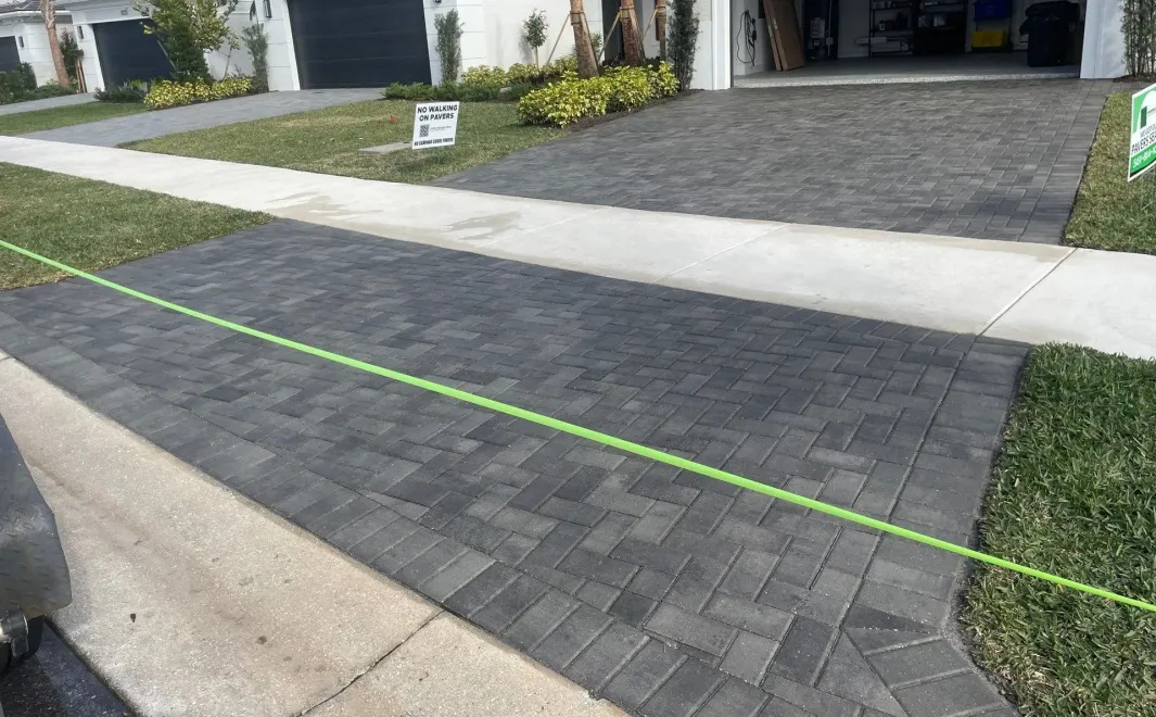 Driveway with gray paver stones, a green alignment string, and a garage entrance in the background