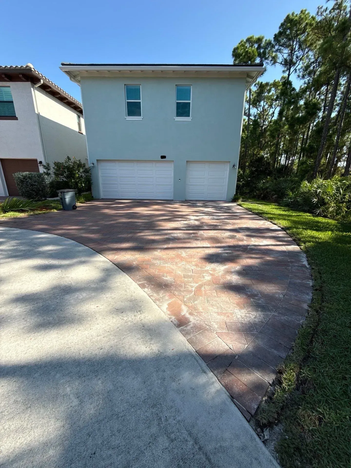 Two-story white house with a double garage and a curved driveway in bright sunlight