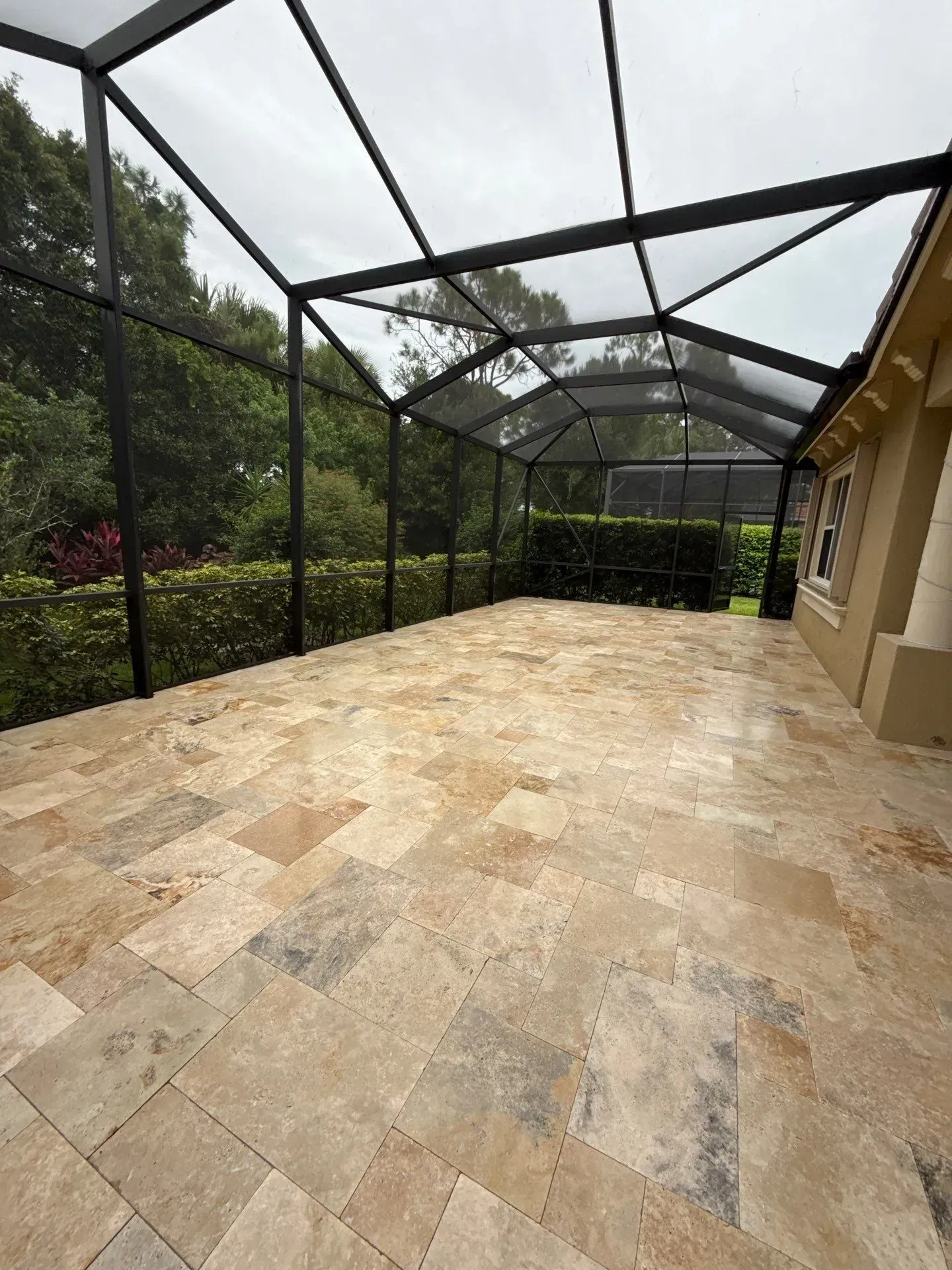 Screened patio with tan stone floor, black metal frame, and lush garden views