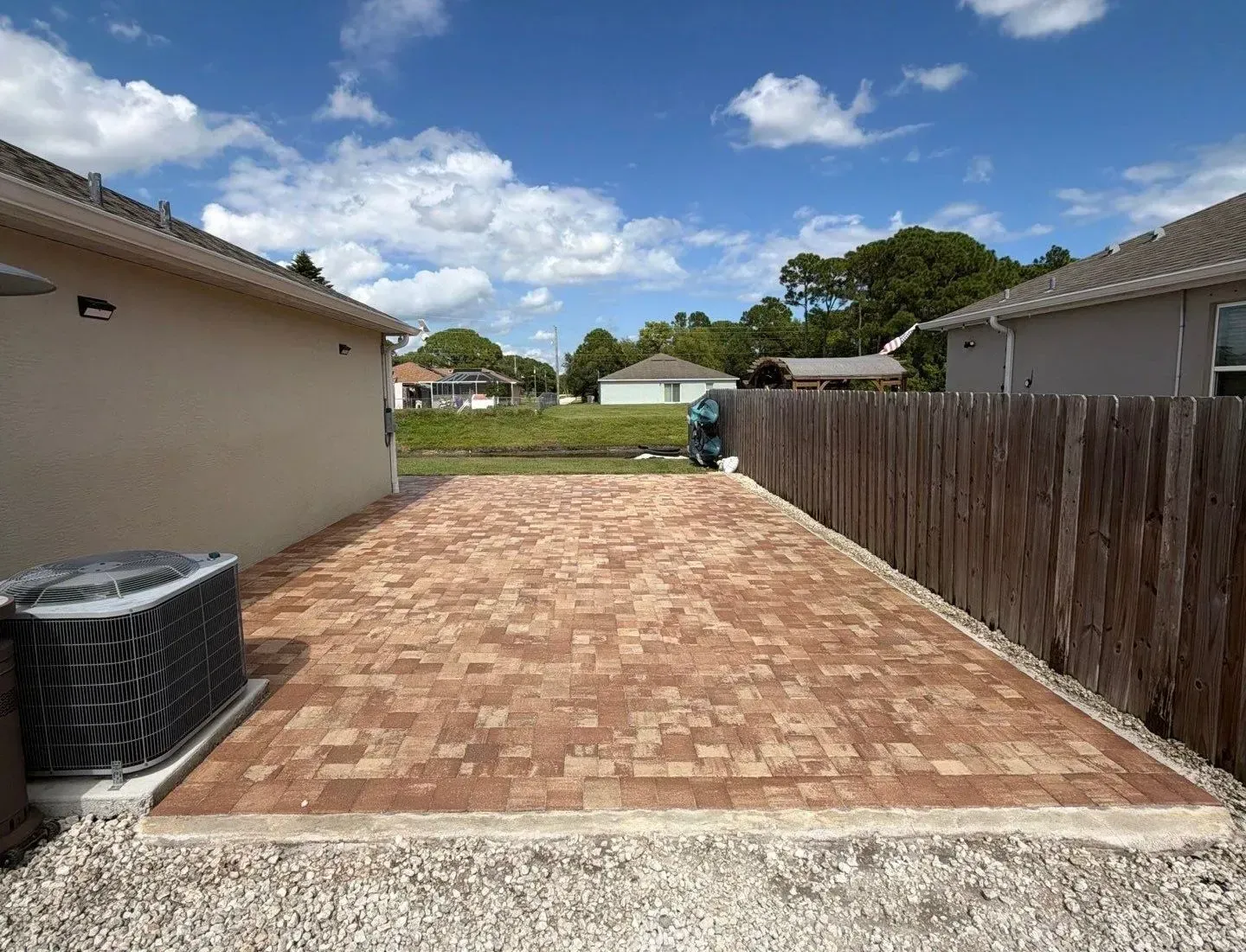 Brick-paved backyard patio between houses under a blue sky with clouds
