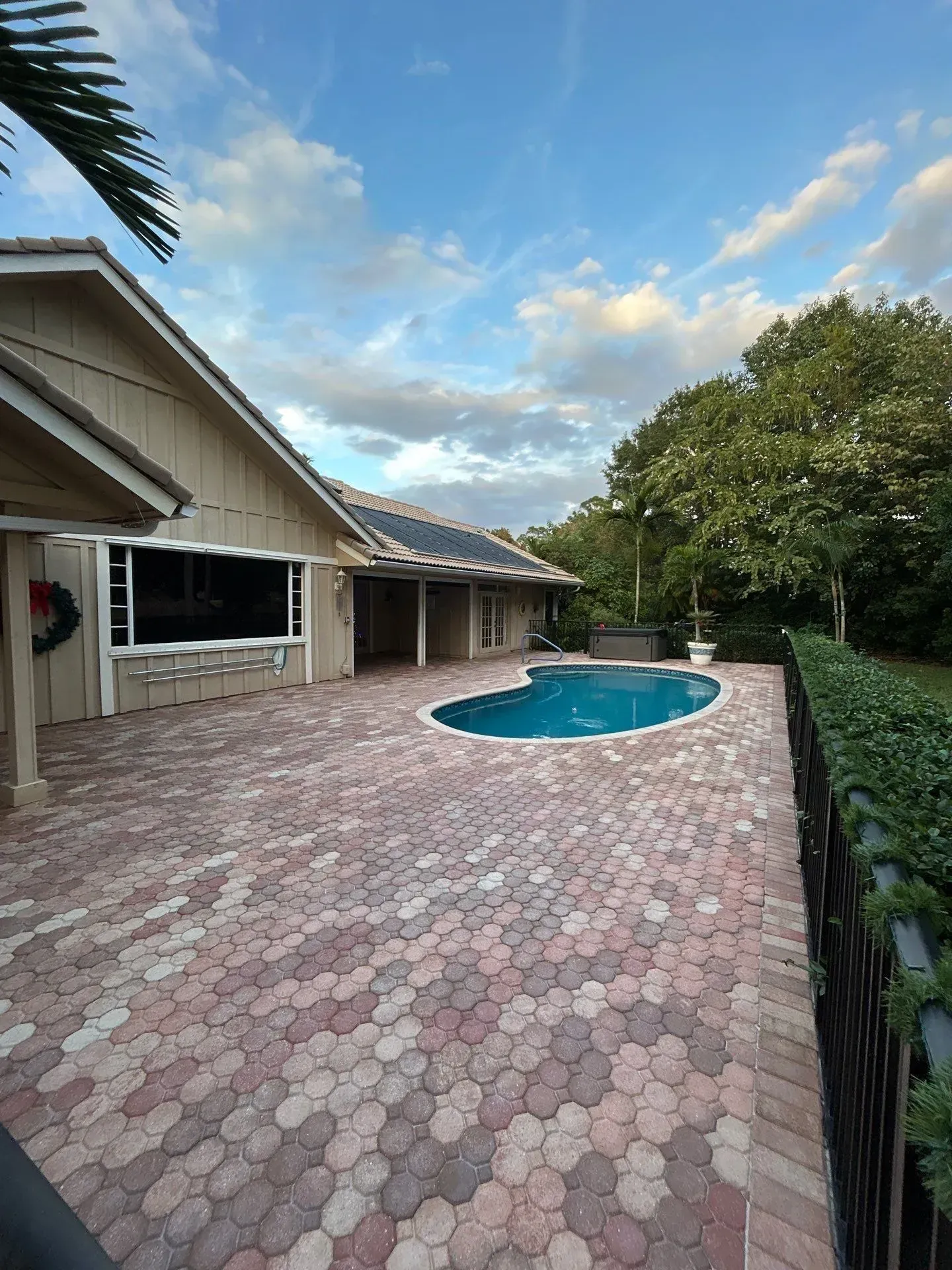 Backyard patio with brick pavers, a small pool, and a house under a cloudy sky