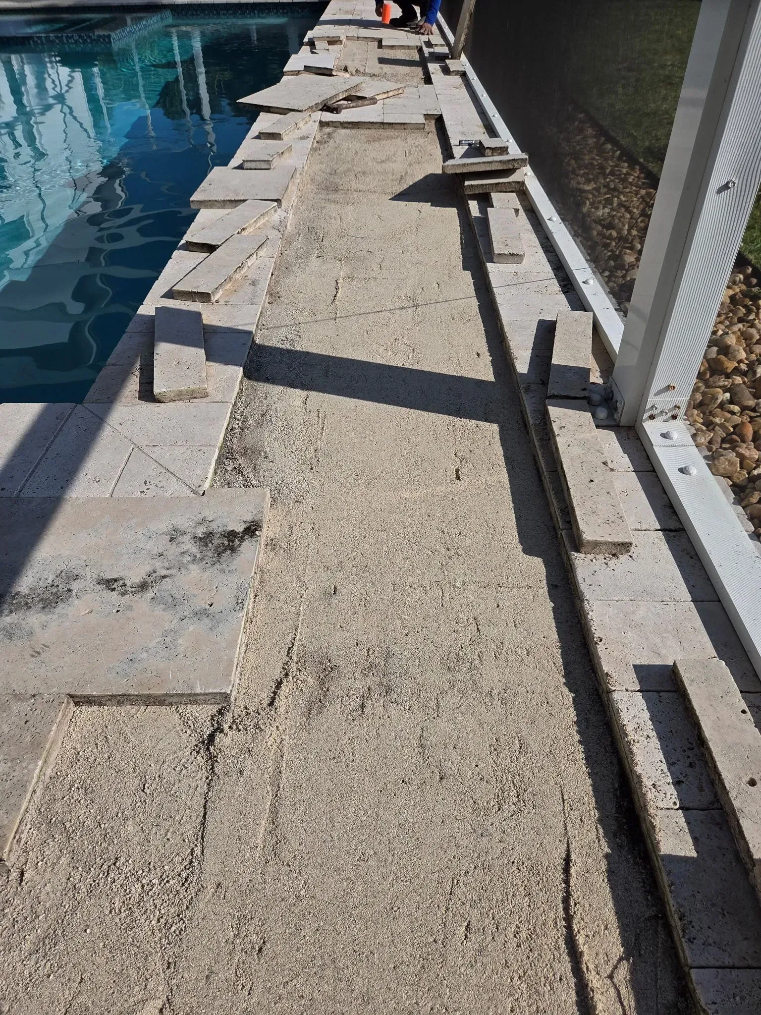 Narrow concrete walkway beside a blue pool, with railings and shadows along the path