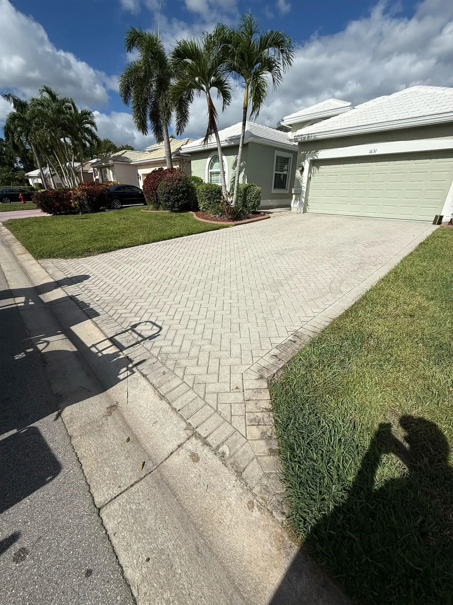 Suburban house with white garage, palm trees, and a light gravel driveway under a bright sky