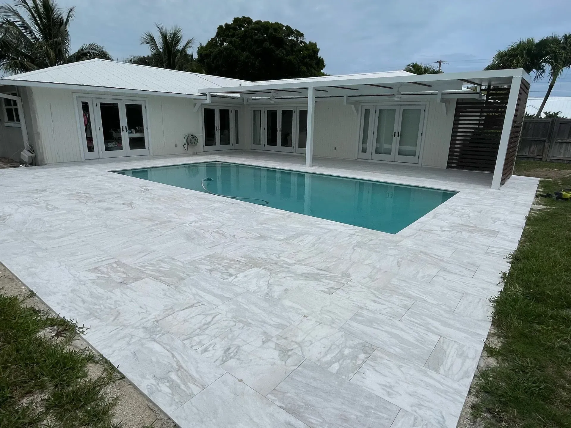 Modern white patio with a rectangular swimming pool beside a white house