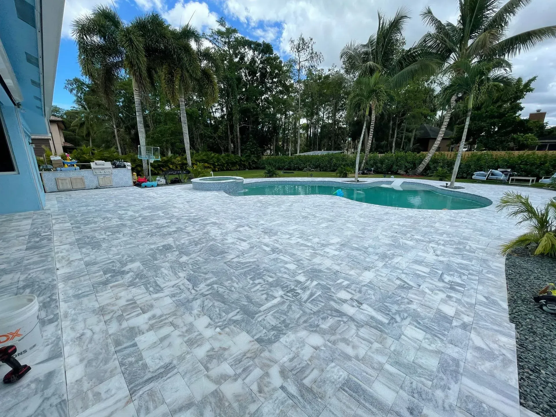 Modern poolside patio with white stone tiles, turquoise pool, palm trees, and a blue sky