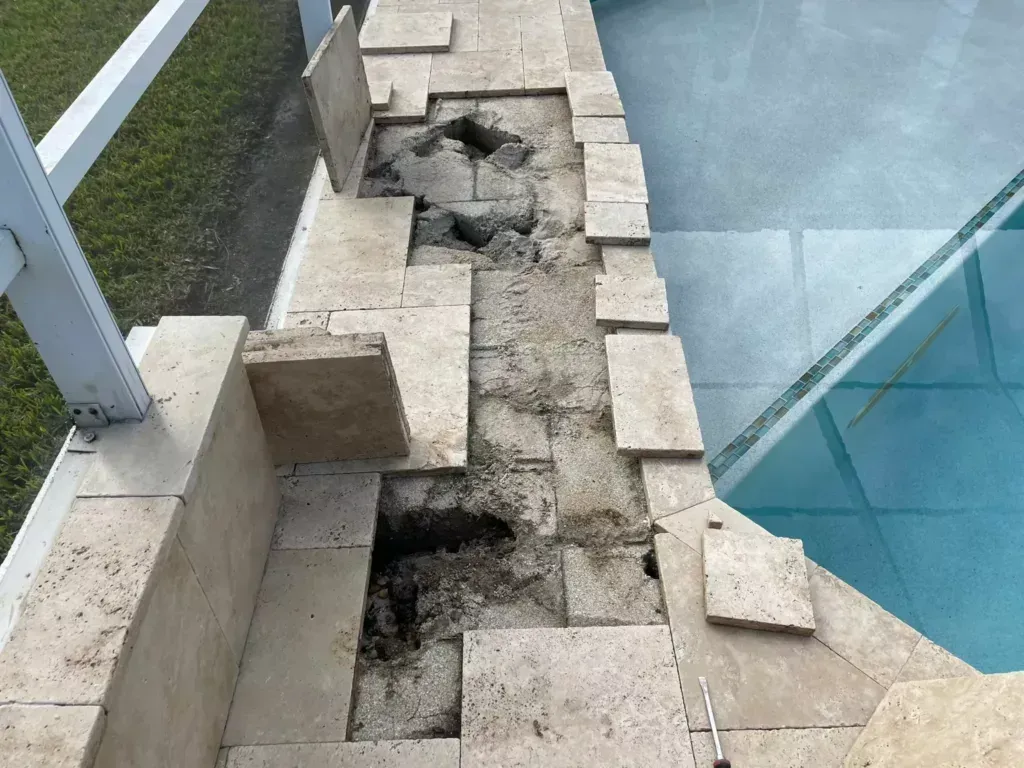 Broken stone walkway beside a glass pool edge with loose pavers and a damaged section