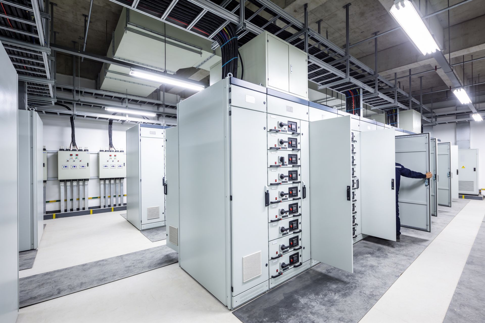 Industrial electrical control cabinets in a bright factory room with open panels and overhead lighting