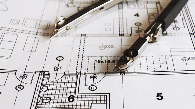 A pair of drafting compasses resting on a detailed black and white architectural floor plan.