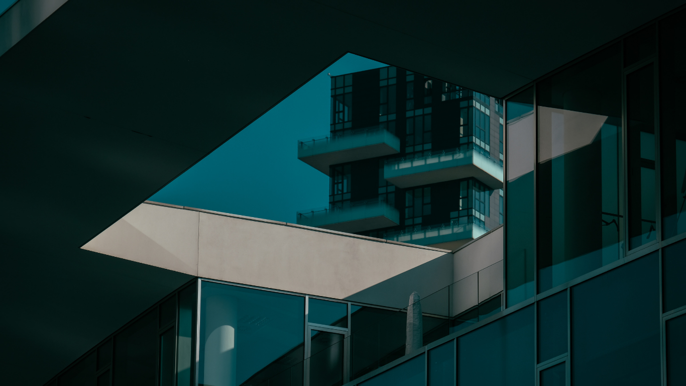 Modern building architecture with deep blue glass, clean geometric lines, and a light gray overhang against a dark sky.