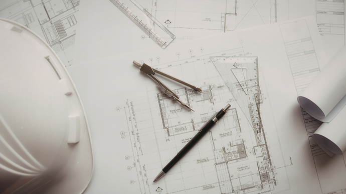 A white hard hat, a compass, and a mechanical pencil arranged on top of construction blueprints.