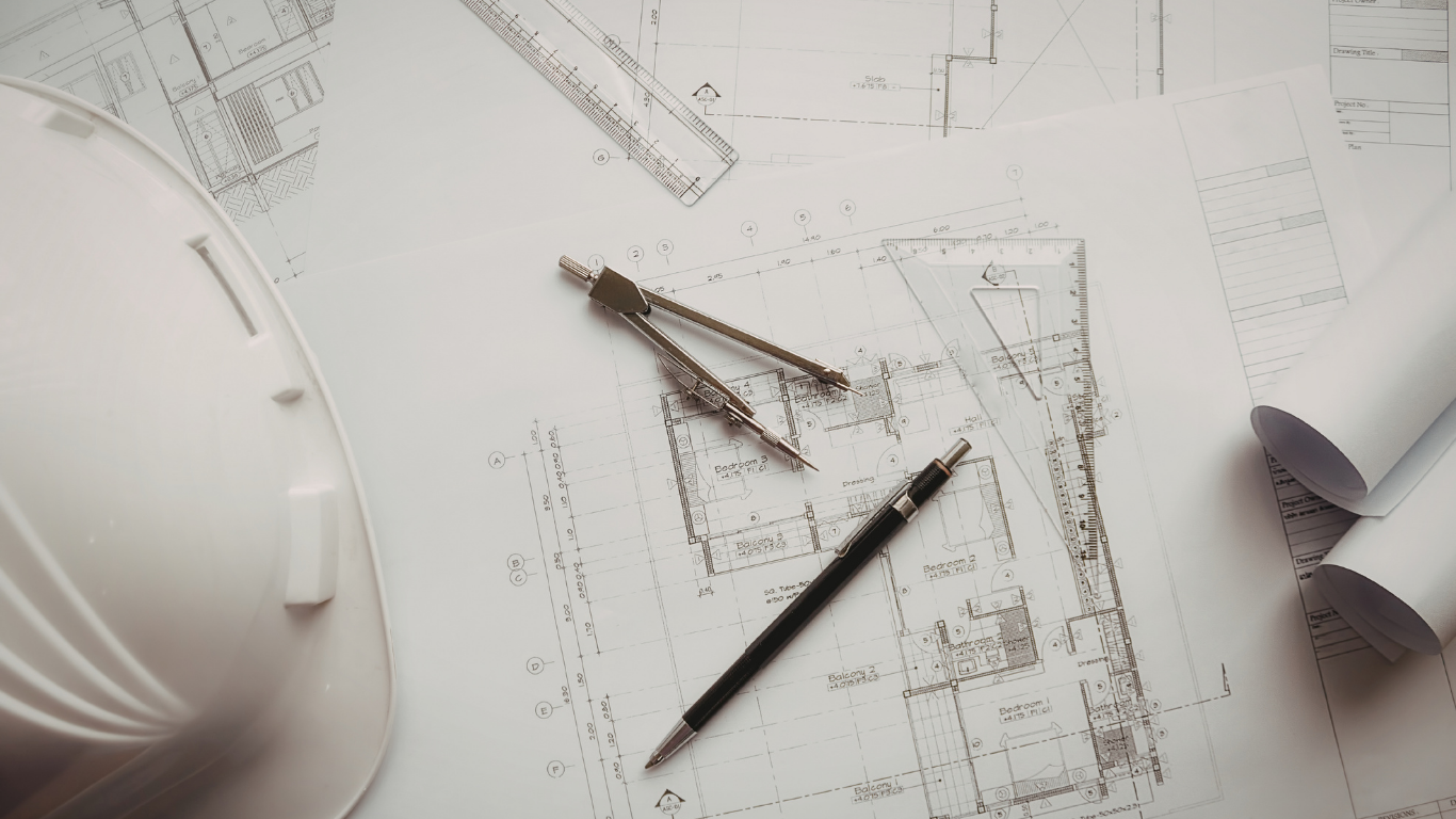 A white hard hat, a compass, and a pencil resting on a set of architectural floor plans.