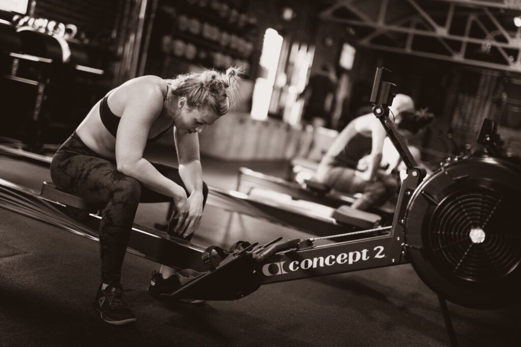 Two athletes resting beside rowing machines in a gym in Reno, NV, one wiping sweat