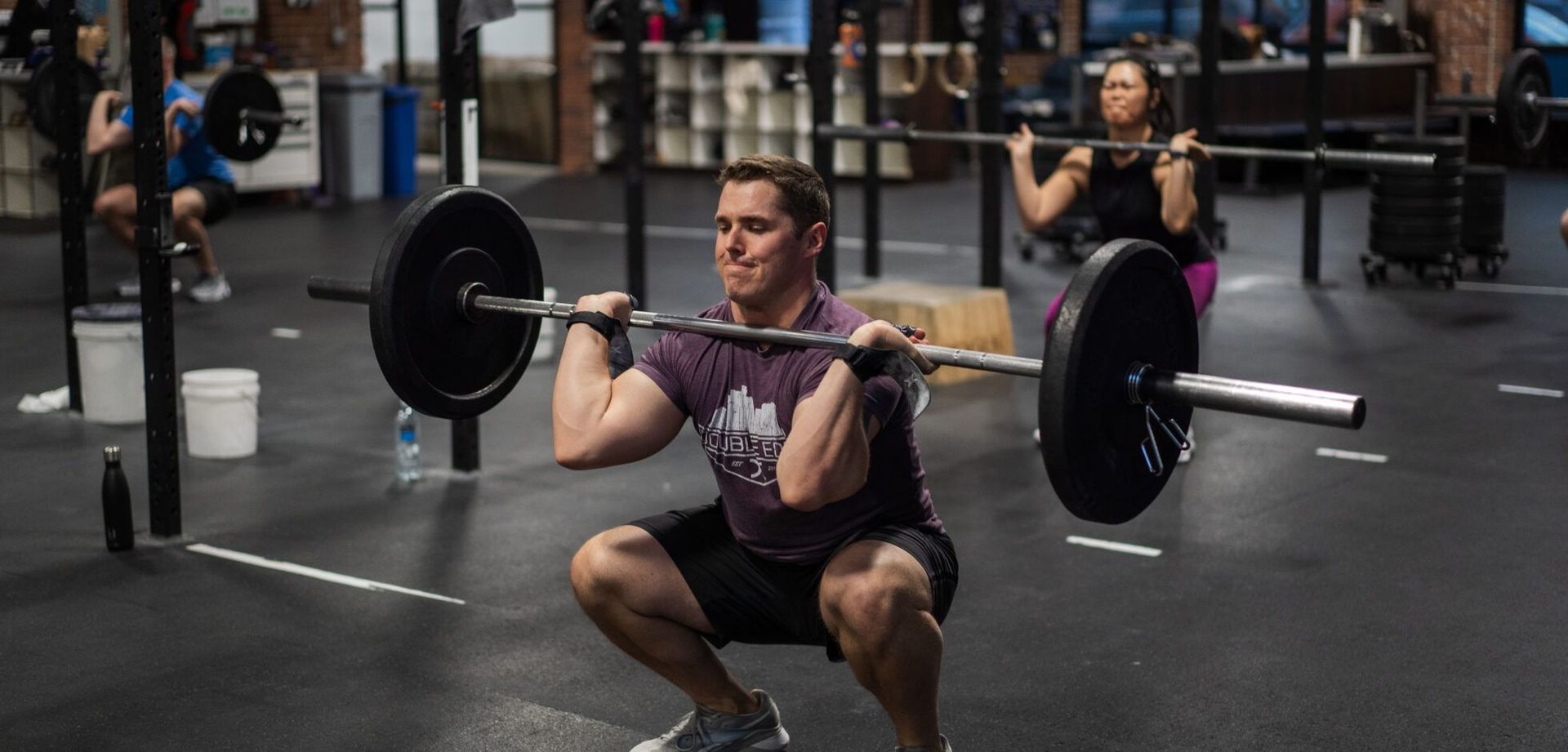 Person performing a front squat with a barbell in a gym in Reno, NV, with people exercising in the background