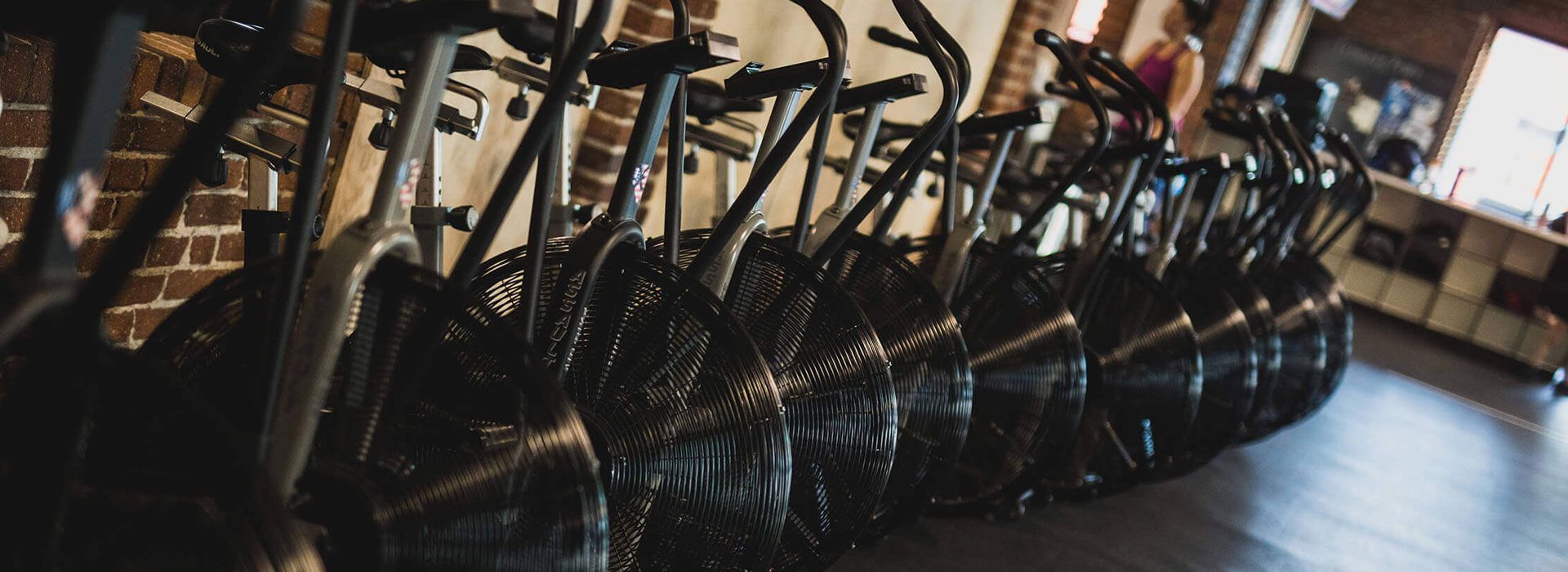 Row of black exercise bikes lined up in a gym studio with wooden floors.