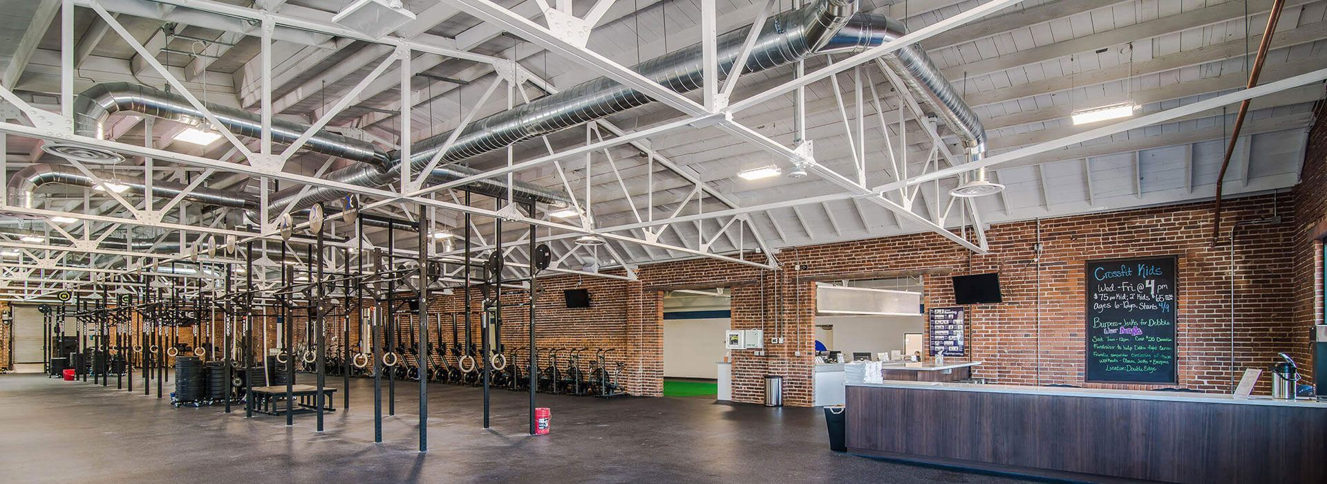 Spacious gym with weight racks, white trusses, brick walls, and a reception desk