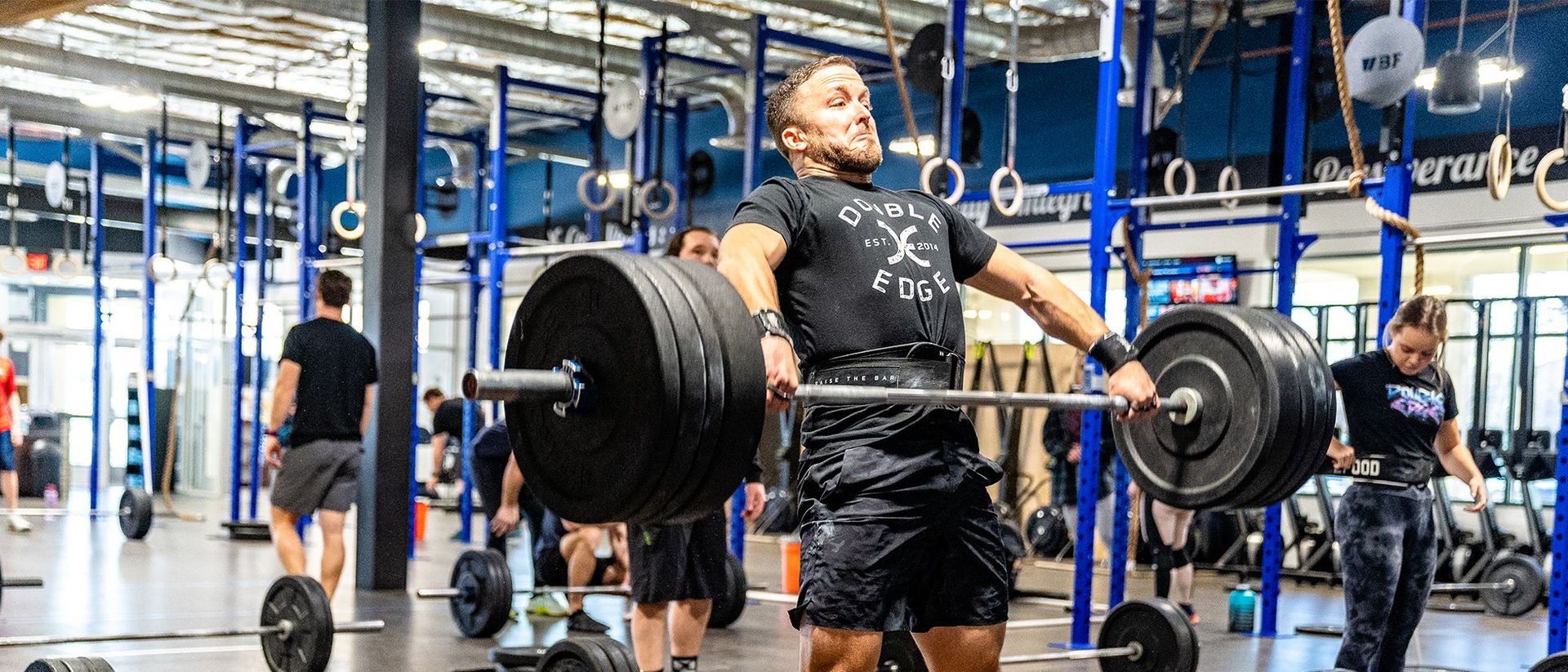 Weightlifter deadlifting a heavy barbell in a gym, with people and equipment in the background