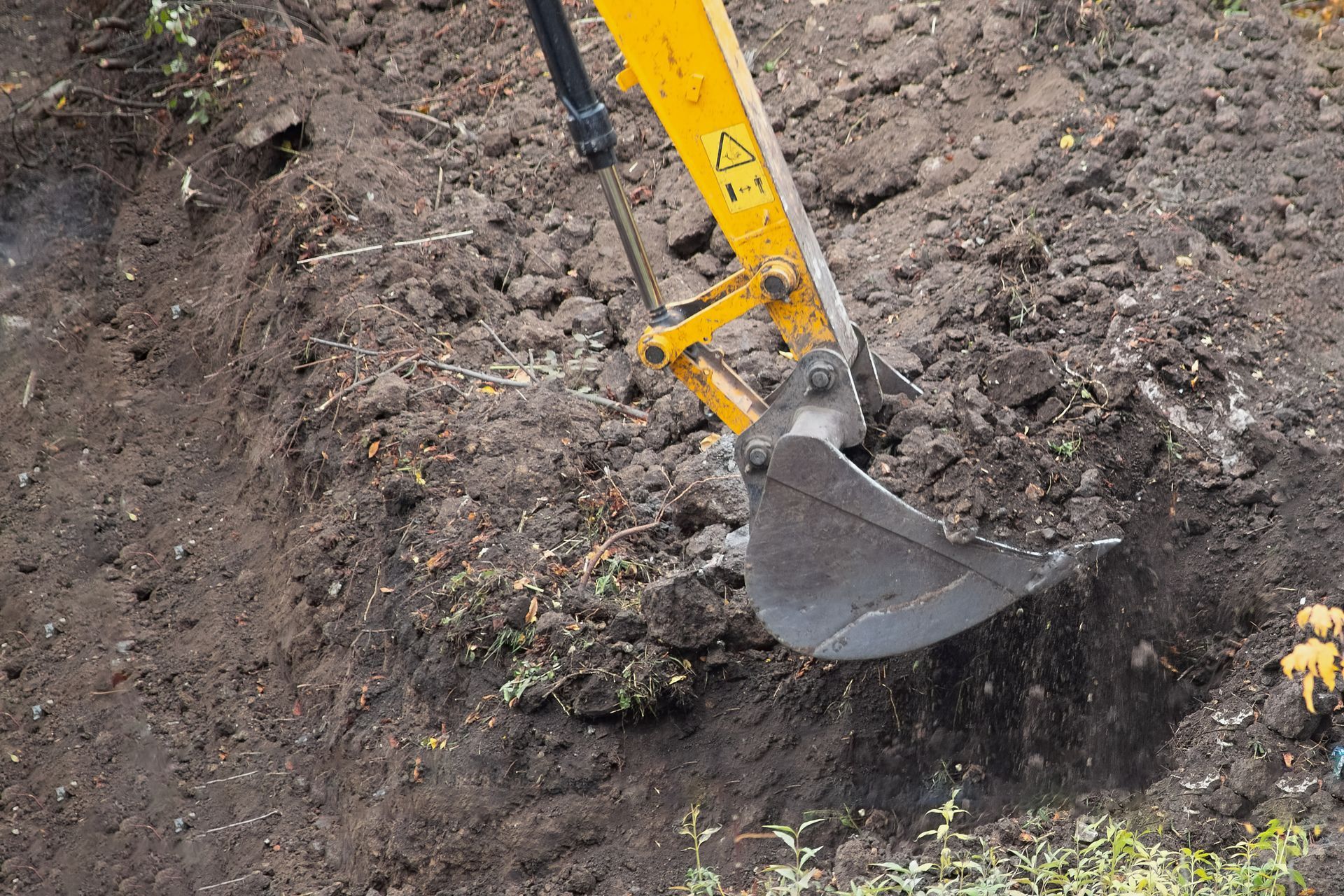 Concrete excavation with an excavator bucket digging into soil.
