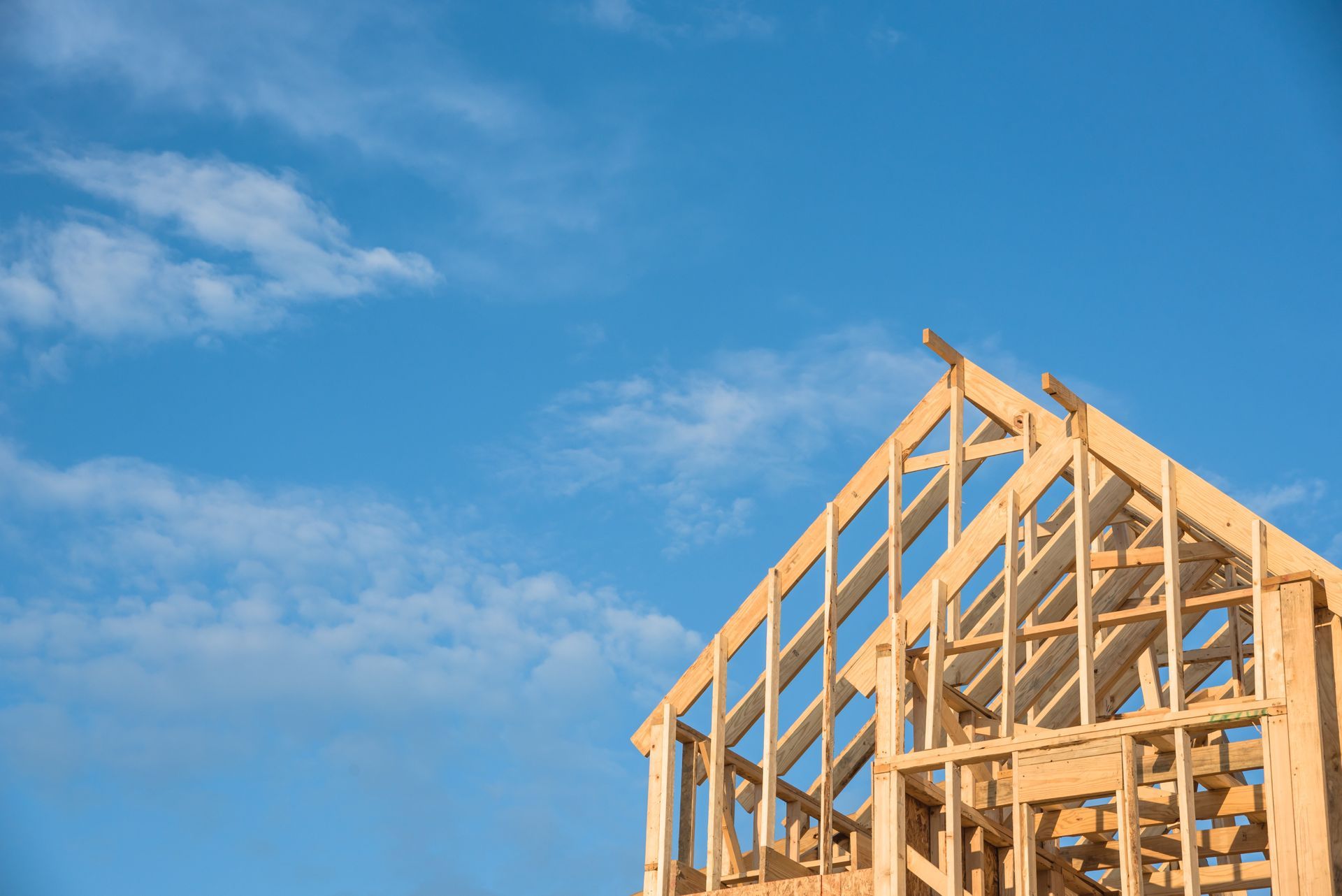 Wooden house framing under construction against a clear blue sky.