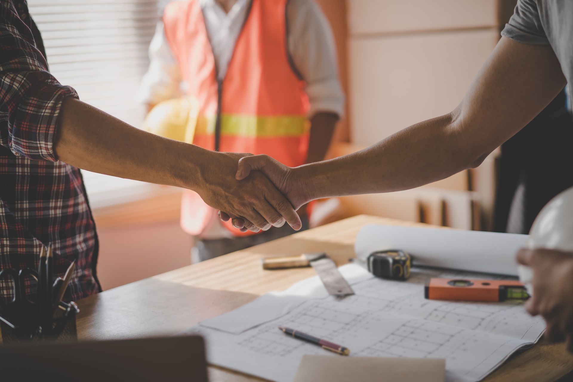 Two people shaking hands over construction plans on a table with tools. Two people shaking hands over construction plans on a table with tools.