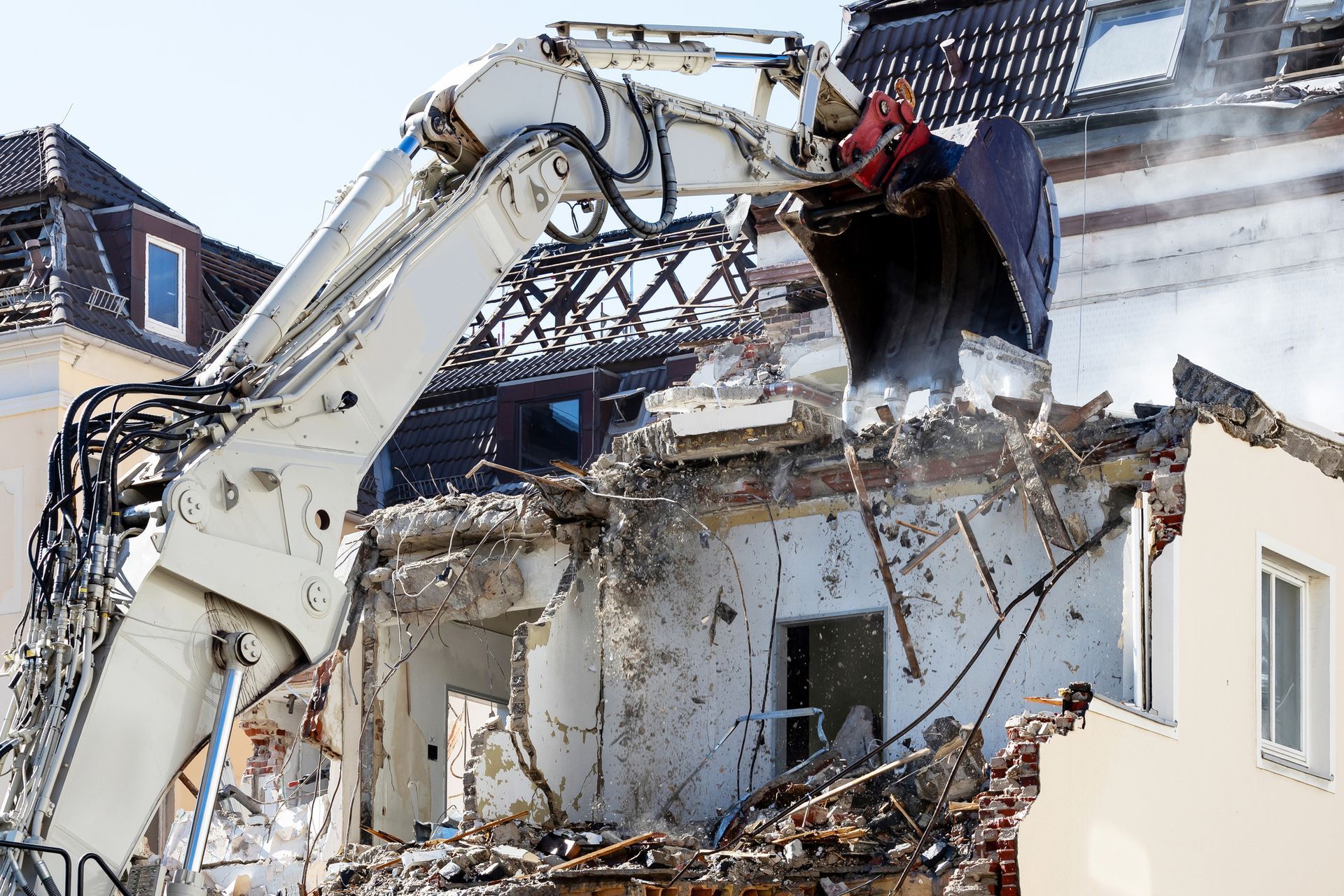 An excavator performing building demolition, tearing down house structure during daytime operation.