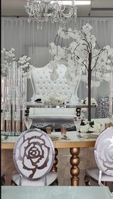Wedding reception setting with white decor and rose-shaped chair backs.