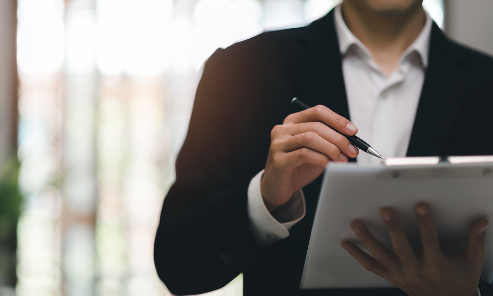 Person in a dark blazer holding a pen and using a tablet in an office setting