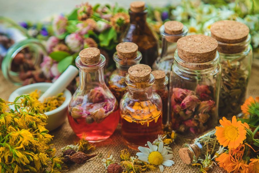 Bottiglie di vetro riempite con infusi di erbe e fiori secchi, disposte insieme a fiori gialli freschi su una superficie di iuta.