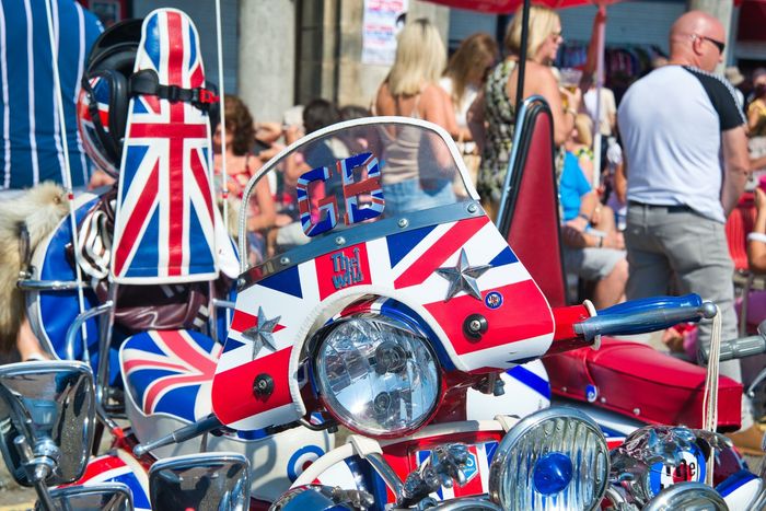 Union Jack–decorated scooter at a crowded outdoor event, with matching red, white, and blue flags.
