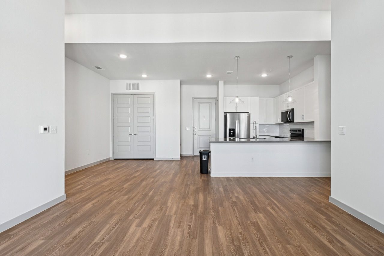 Open-concept living area with kitchen island, stainless appliances, and light wood flooring  at Ennova Fulshear in Fulshear, TX.