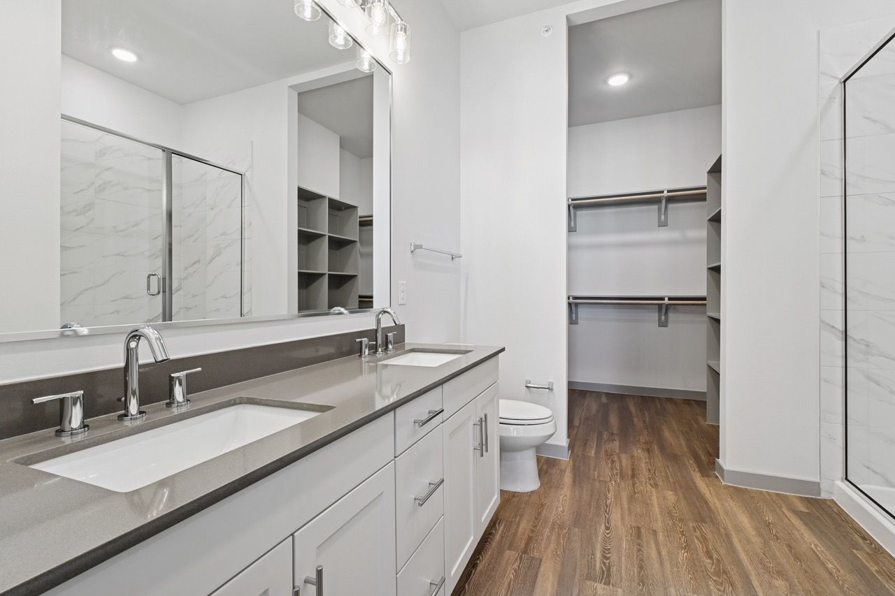 Modern bathroom with double vanity, large mirror, and walk-in closet in a bright apartment  at Ennova Fulshear in Fulshear, TX.