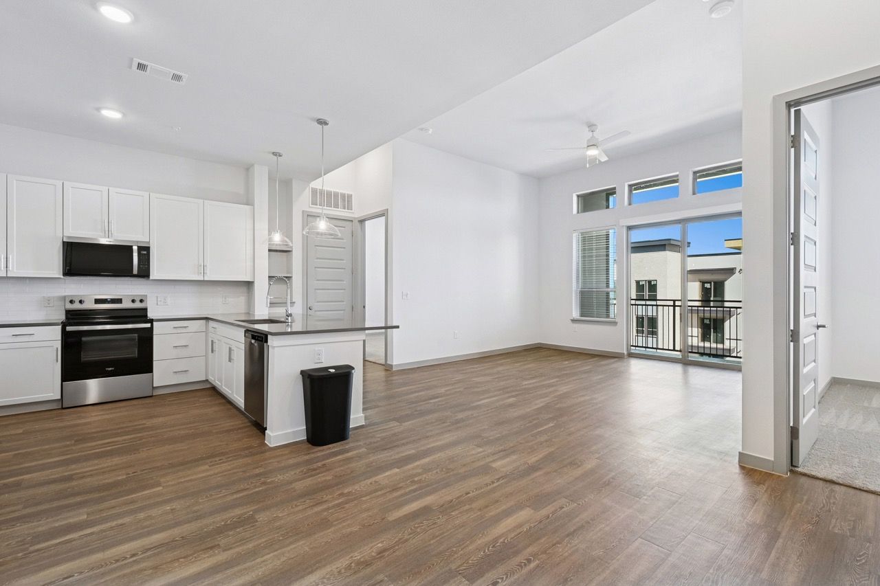 Open kitchen and living area with white cabinets, stainless-steel appliances, island, and large windows  at Ennova Fulshear in Fulshear, TX.