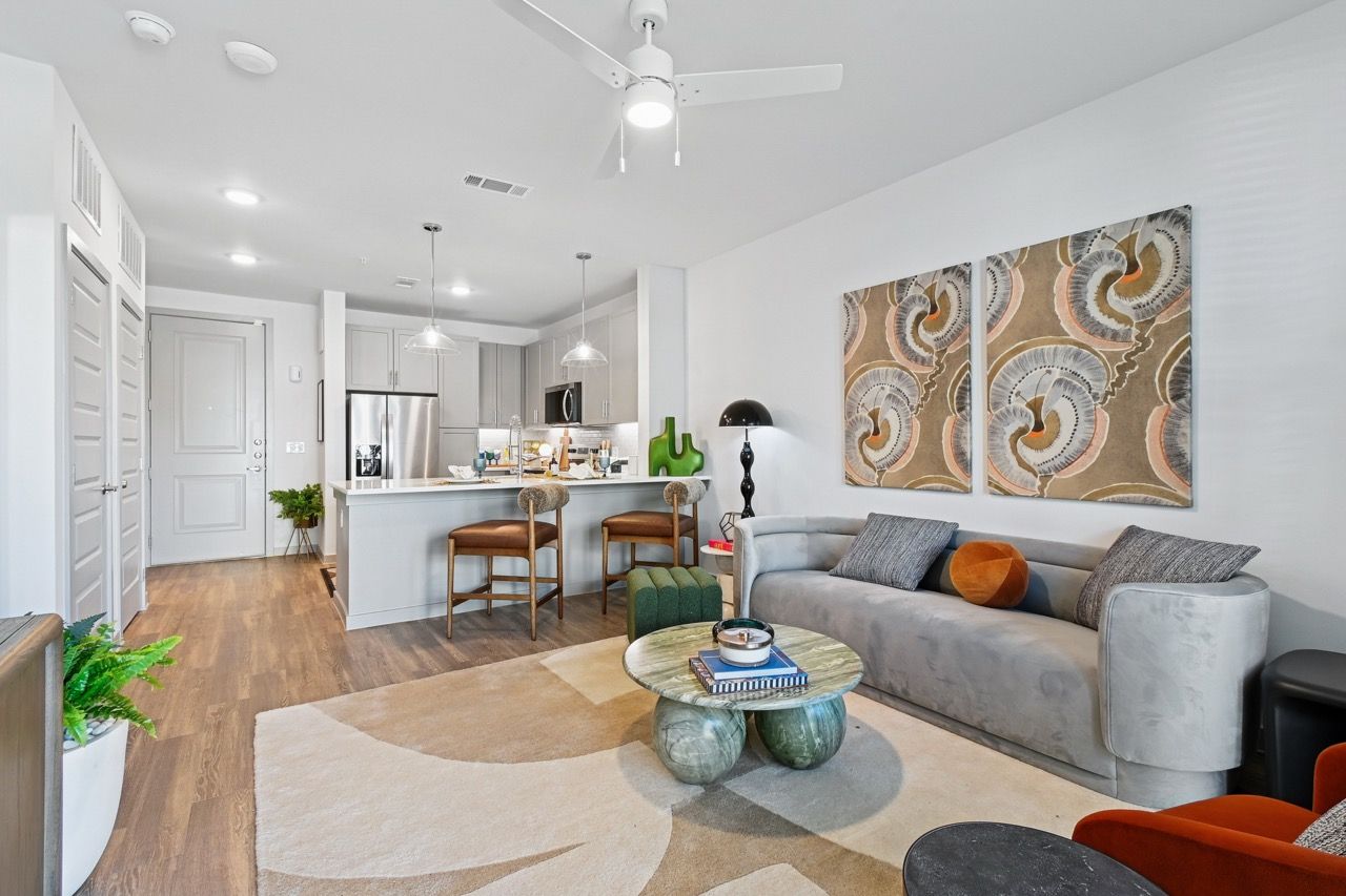 Open-concept living room with a gray sofa, round coffee table, and a kitchen island  at Ennova Fulshear in Fulshear, TX.