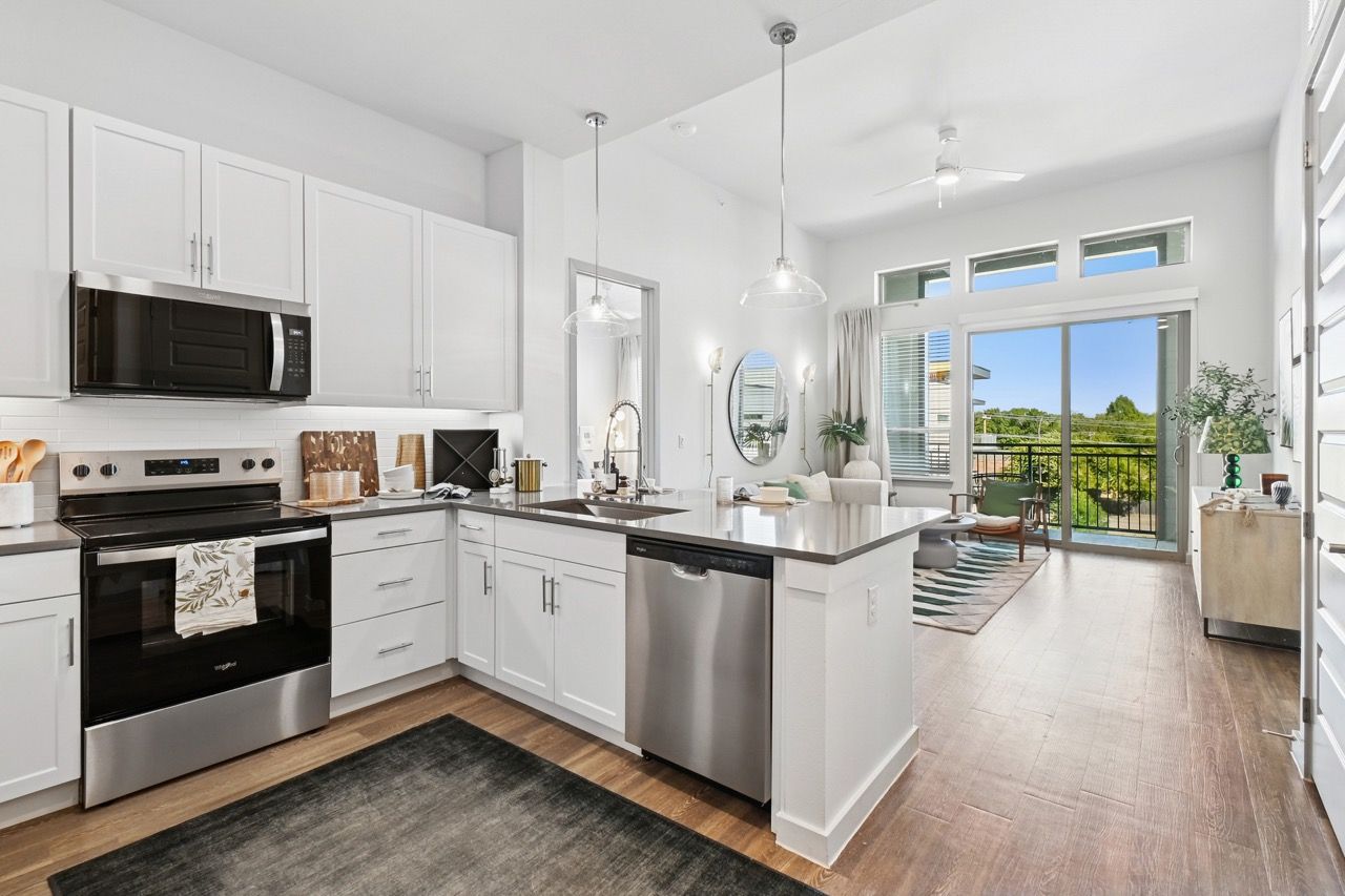 Bright white kitchen with stainless steel appliances and an island, open to living area with balcony    at Ennova Fulshear in Fulshear, TX.