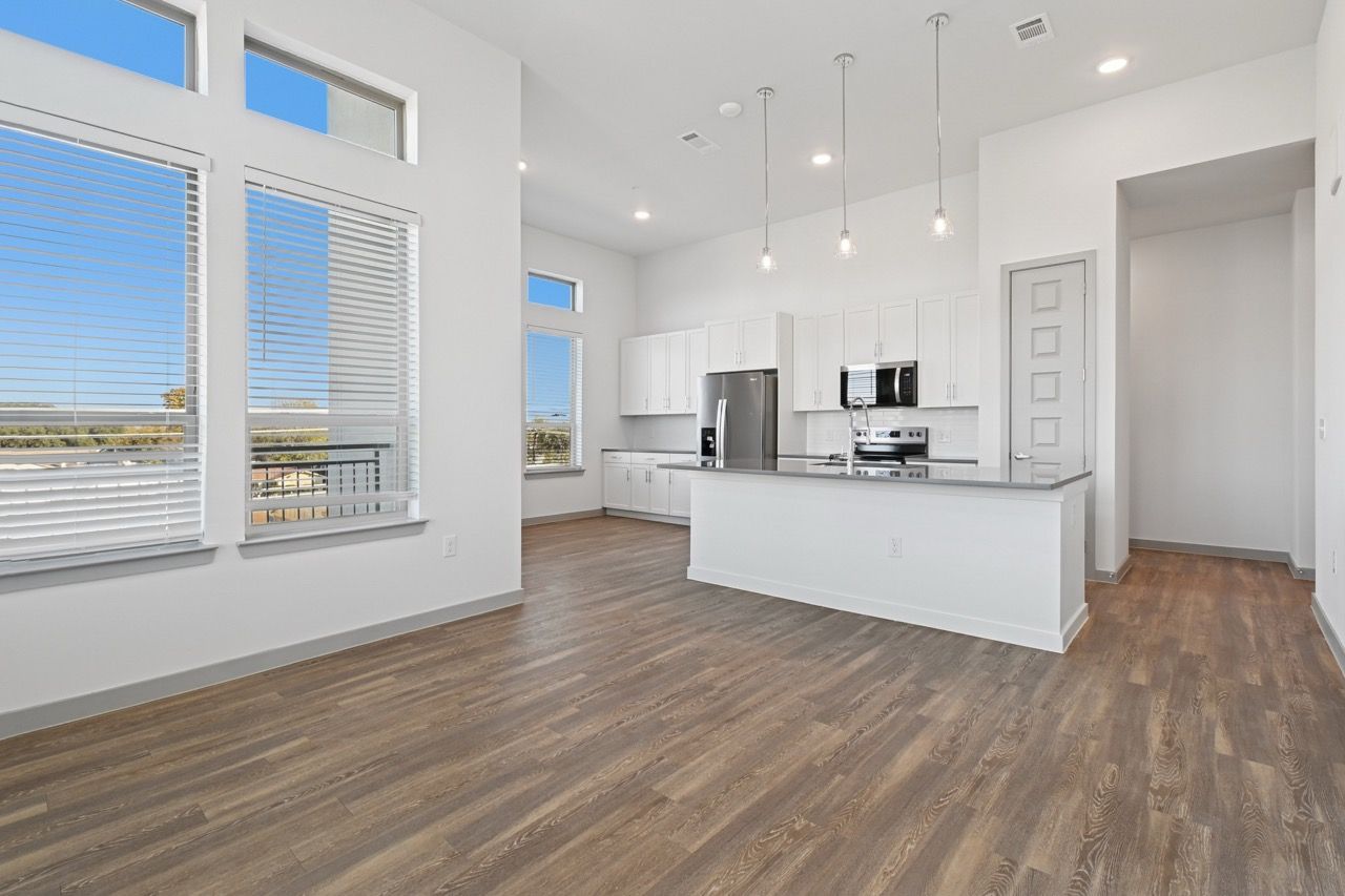 Open-concept kitchen in a modern apartment with white cabinets, stainless steel appliances  at Ennova Fulshear in Fulshear, TX.